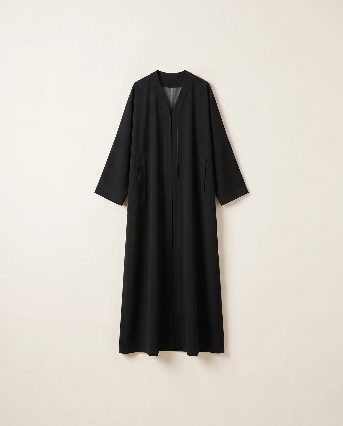 A black nida crepe abaya, straight cut, on a pale ground